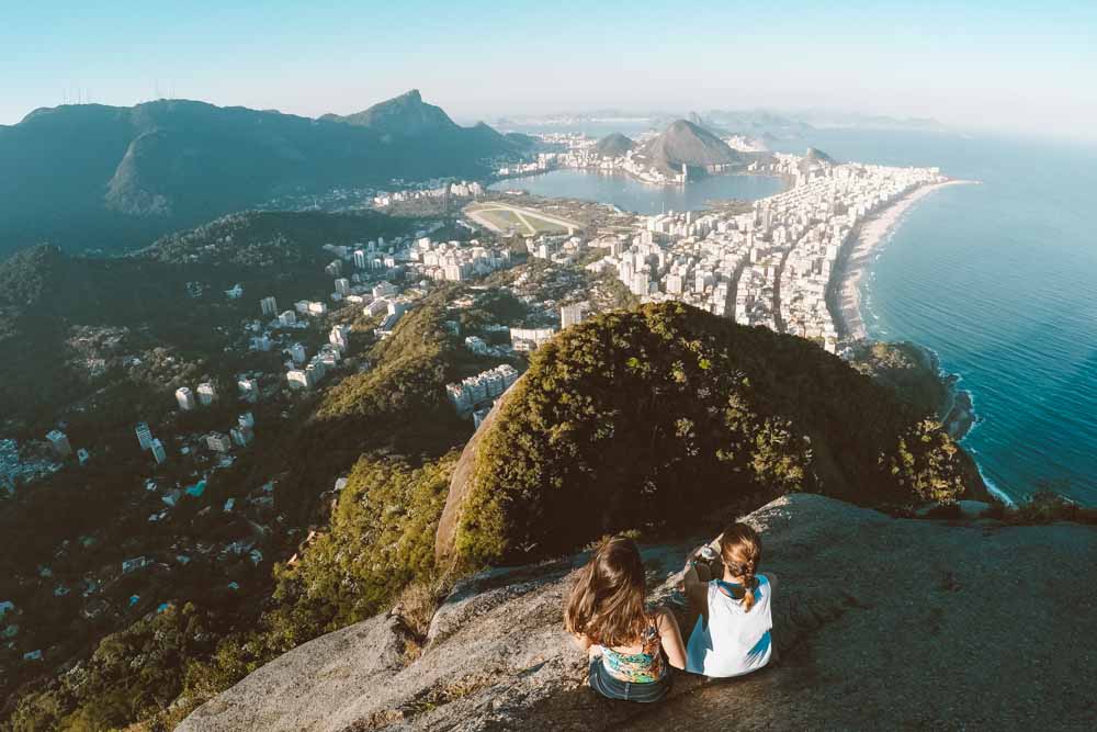 Imagem de duas mulheres sentadas de frente à uma vista que mostra a cidade do rio de janeiro.